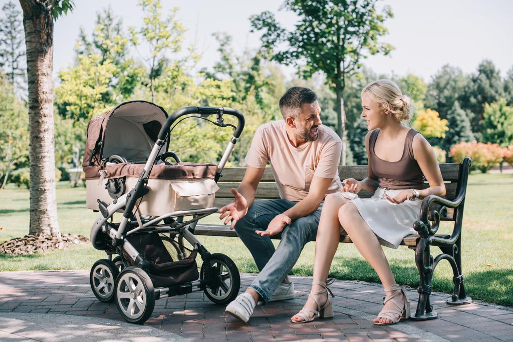 parents quarreling on bench near baby carriage in park - Photo, Image