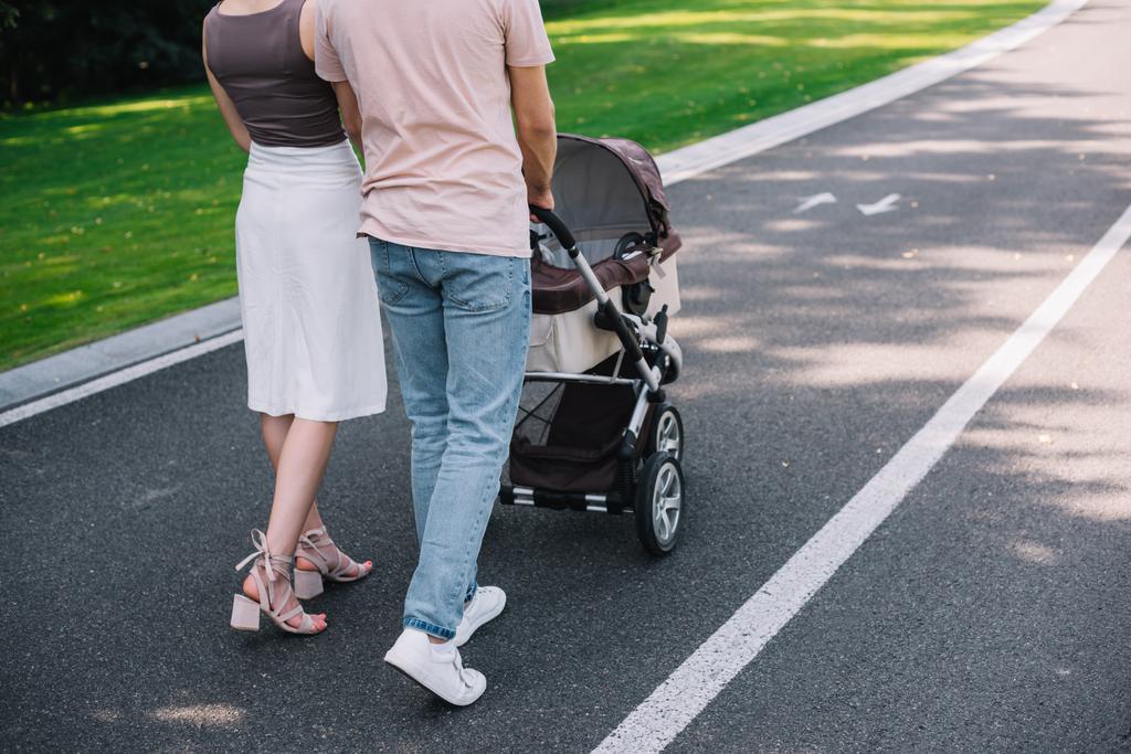 cropped image of parents walking with baby carriage on road in park - Photo, Image