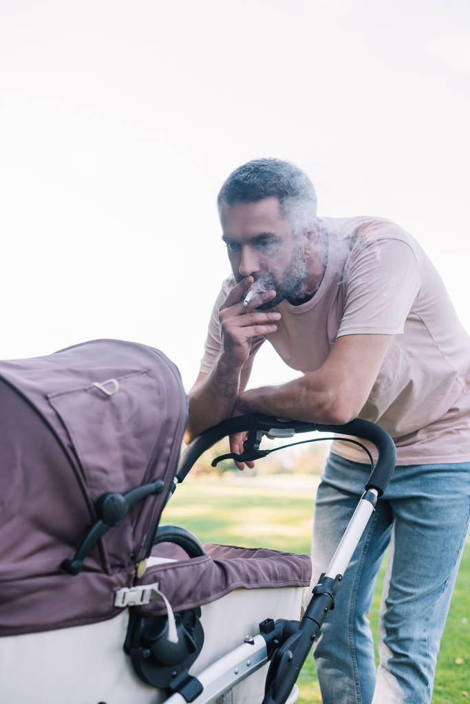 père fumer cigarette près de bébé landau dans le parc
 - Photo, image