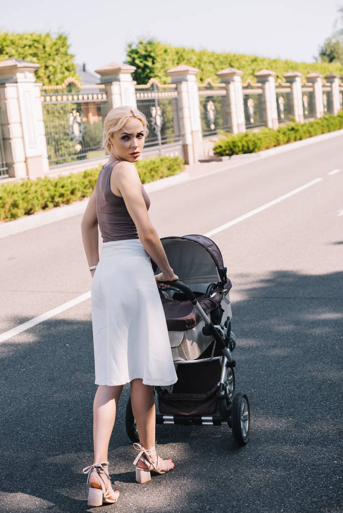 back view of irritated mother walking with baby carriage in park - Photo, Image