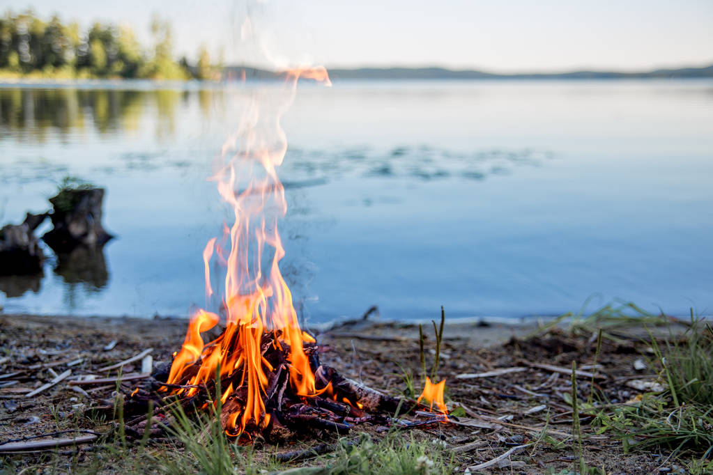 schönes Lagerfeuer am Abend am See. Feuer brennt in der Dämmerung auf einem Campingplatz in der Nähe eines Flusses in schöner Natur - Foto, Bild