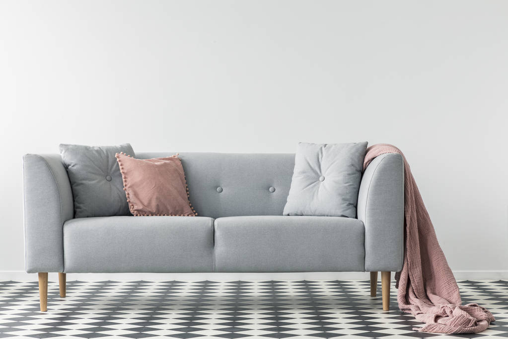 Cobertor rosa no sofá cinza com almofadas no chão quadriculado no interior da sala de estar branca. Foto real
 - Foto, Imagem