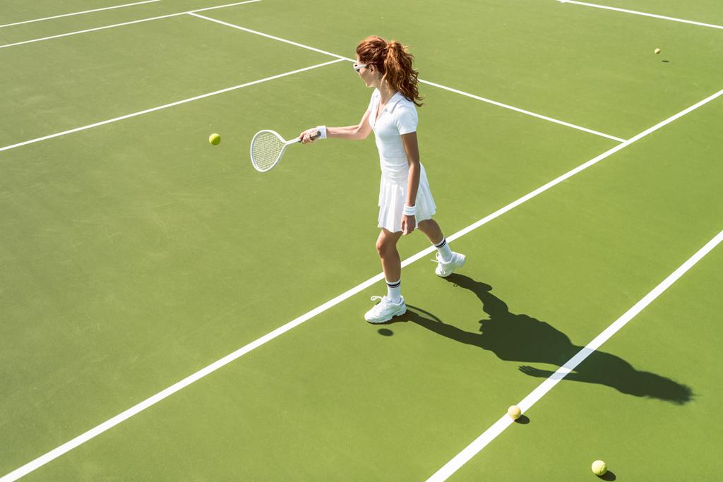 side view of young attractive woman in white tennis uniform playing tennis on court - Photo, Image