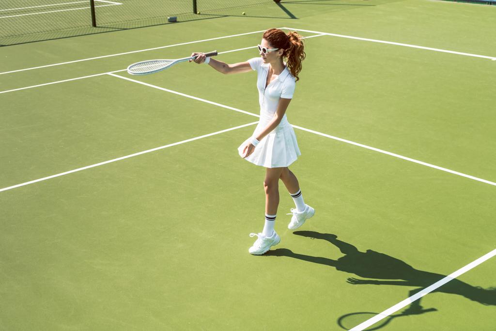 νεαρή γυναίκα τενίστας σε γυαλιά ηλίου παίζοντας τένις στο γήπεδο - Φωτογραφία, εικόνα