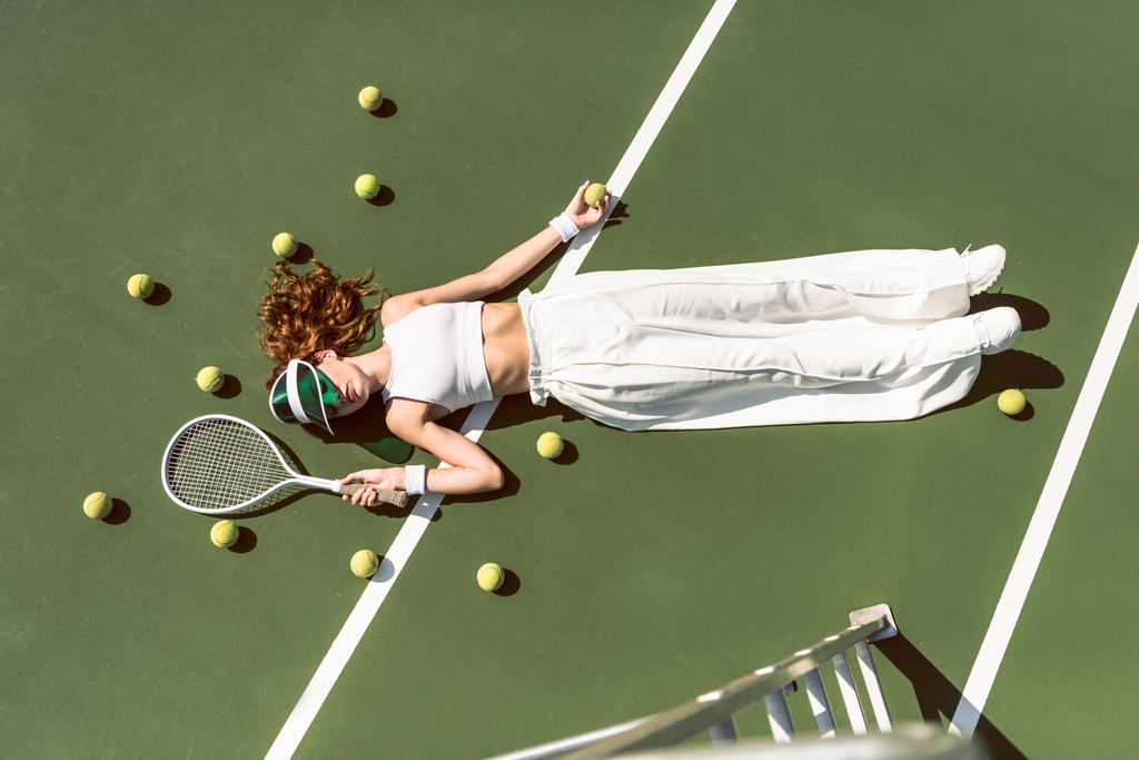 白い服とラケット テニス裁判所に横たわっているラケットで横になっているキャップでスタイリッシュな女性のオーバー ヘッド ビュー - 写真・画像
