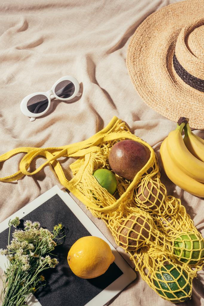 vue de dessus de chapeau de paille, lunettes de soleil, fleurs, tablette numérique et sac à ficelle avec des fruits mûrs
 - Photo, image