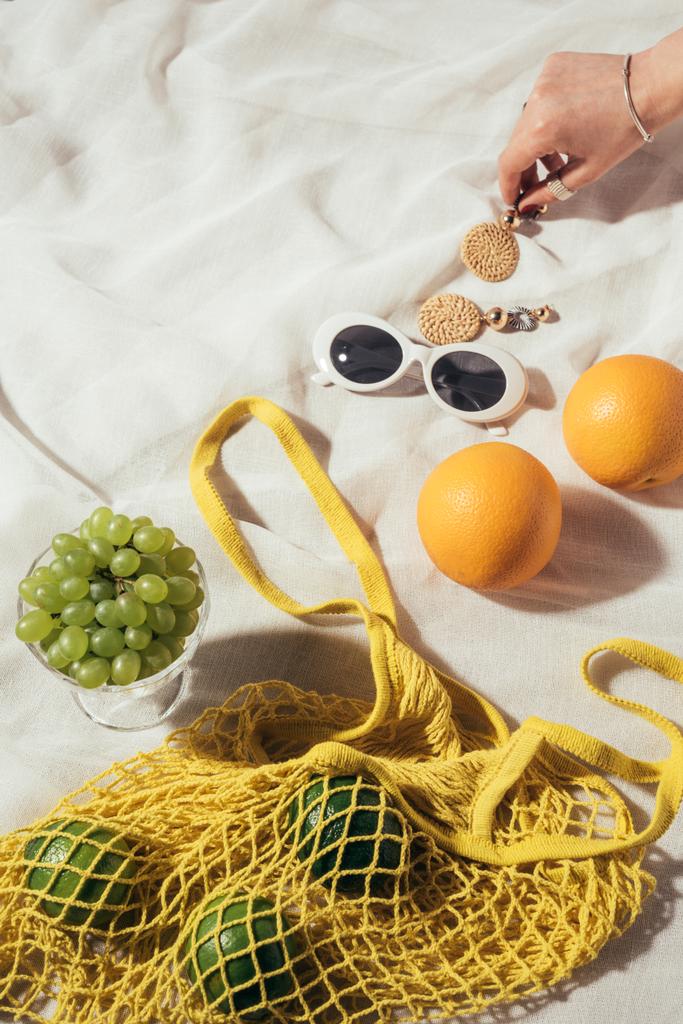 plan recadré de main humaine, boucles d'oreilles, lunettes de soleil et sac à ficelle avec des fruits frais
 - Photo, image