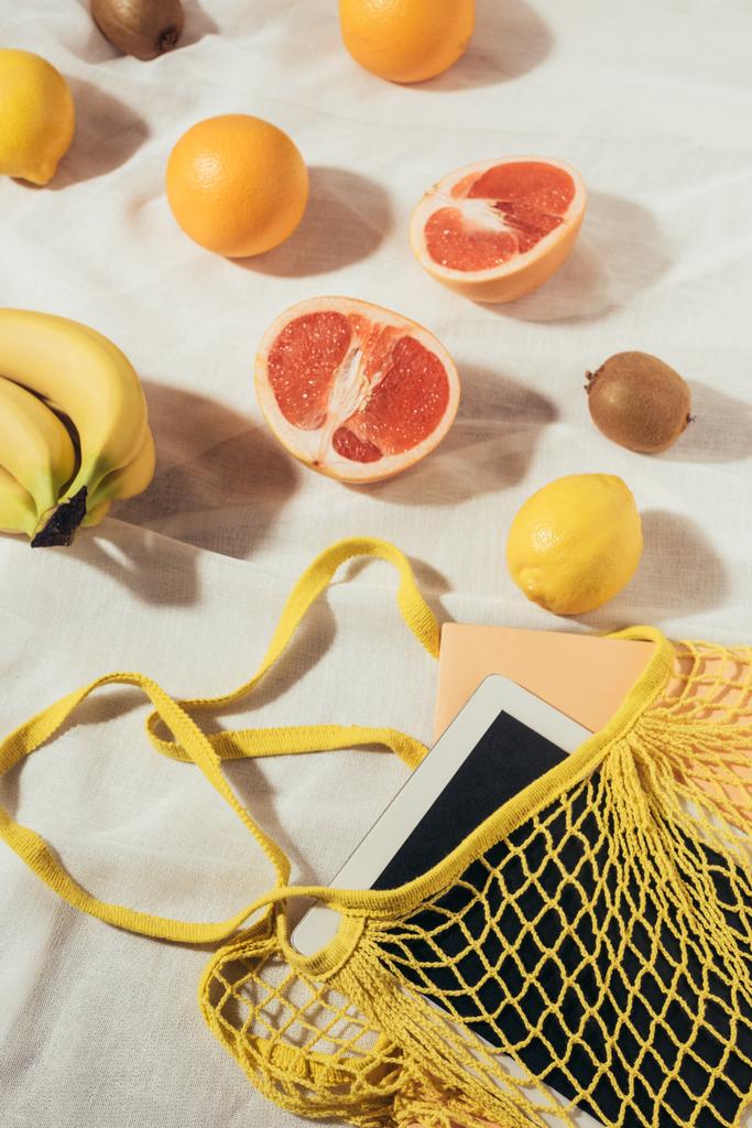 vista superior de la bolsa de hilo amarillo con tableta digital y frutas tropicales frescas maduras
 - Foto, imagen