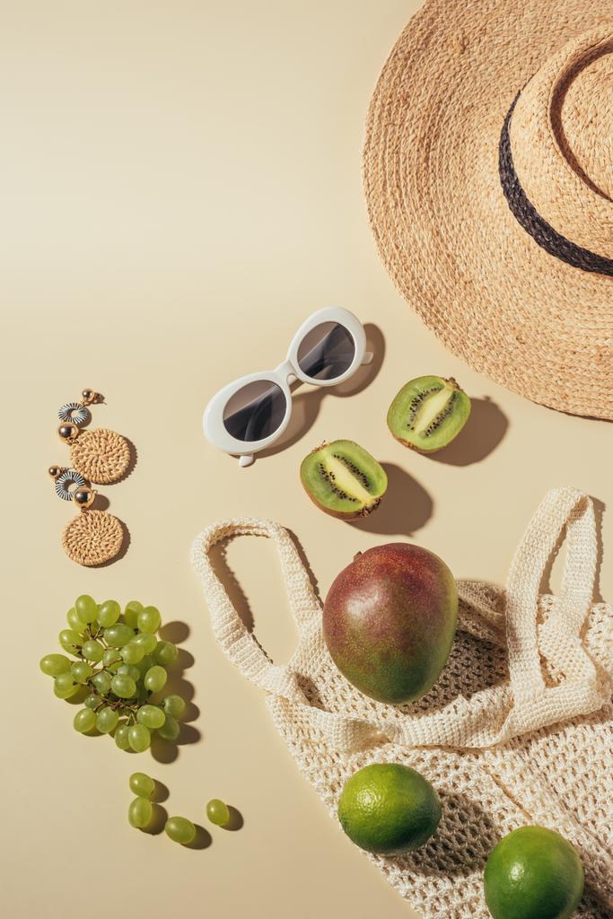 vue de dessus du chapeau en osier, des lunettes de soleil, des boucles d'oreilles et du sac à ficelle avec des fruits frais
  - Photo, image