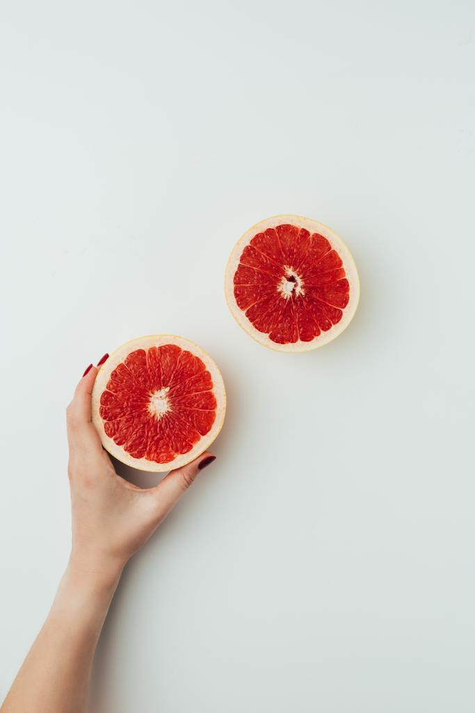 gedeeltelijke weergave van vrouw met grapefruit helften, op grijs - Foto, afbeelding