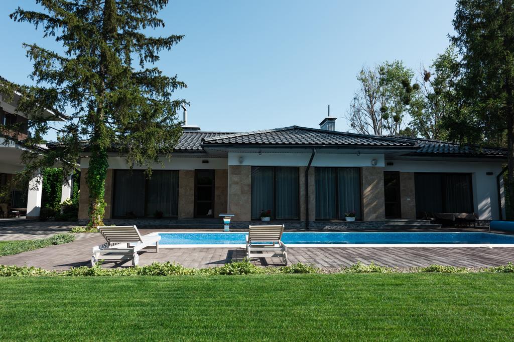 вид на сучасний будинок, біля басейну з сонячними ліжками і зеленим газоном
 - Фото, зображення