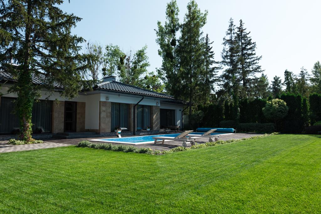 ulkona näkymä moderni talo, vihreä nurmikko ja uima-allas aurinkotuoleja
  - Valokuva, kuva
