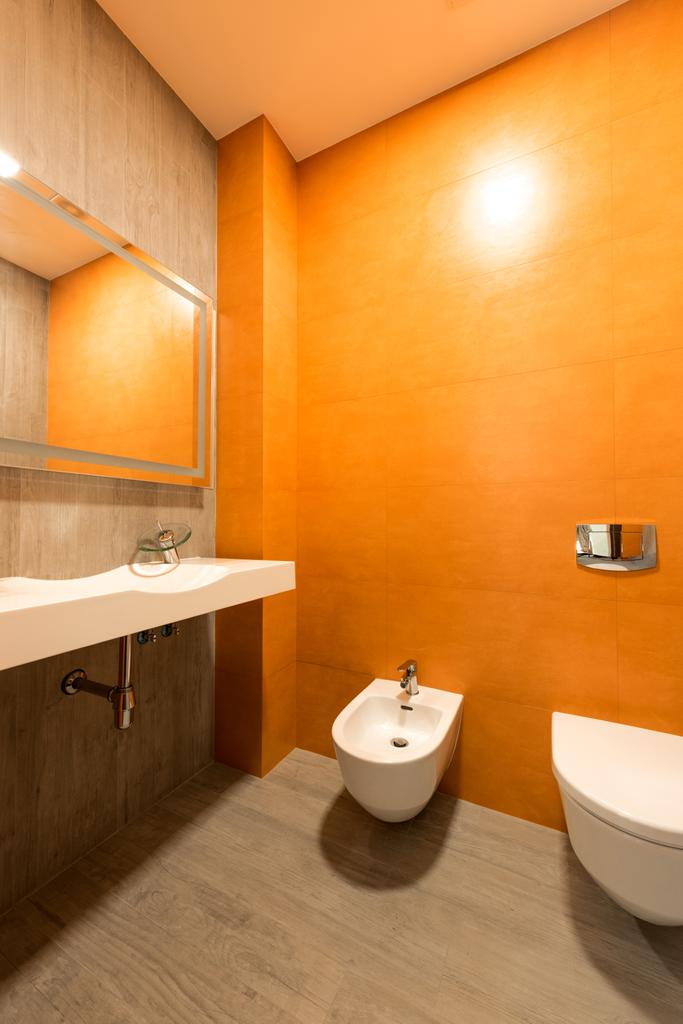 інтер'єр сучасної ванної в помаранчевому і білому кольорах з туалетом і біде
 - Фото, зображення