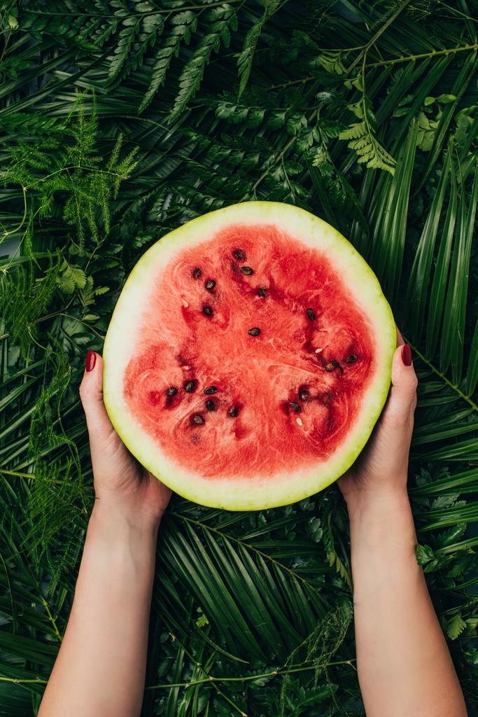 cropped view of woman holding half of sweet red watermelon on palm leaves - Photo, Image