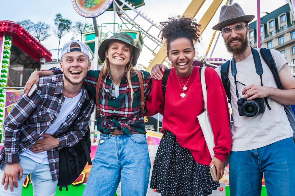 cheerful young multiethnic friends standing together and smiling at camera in amusement park  - Photo, Image