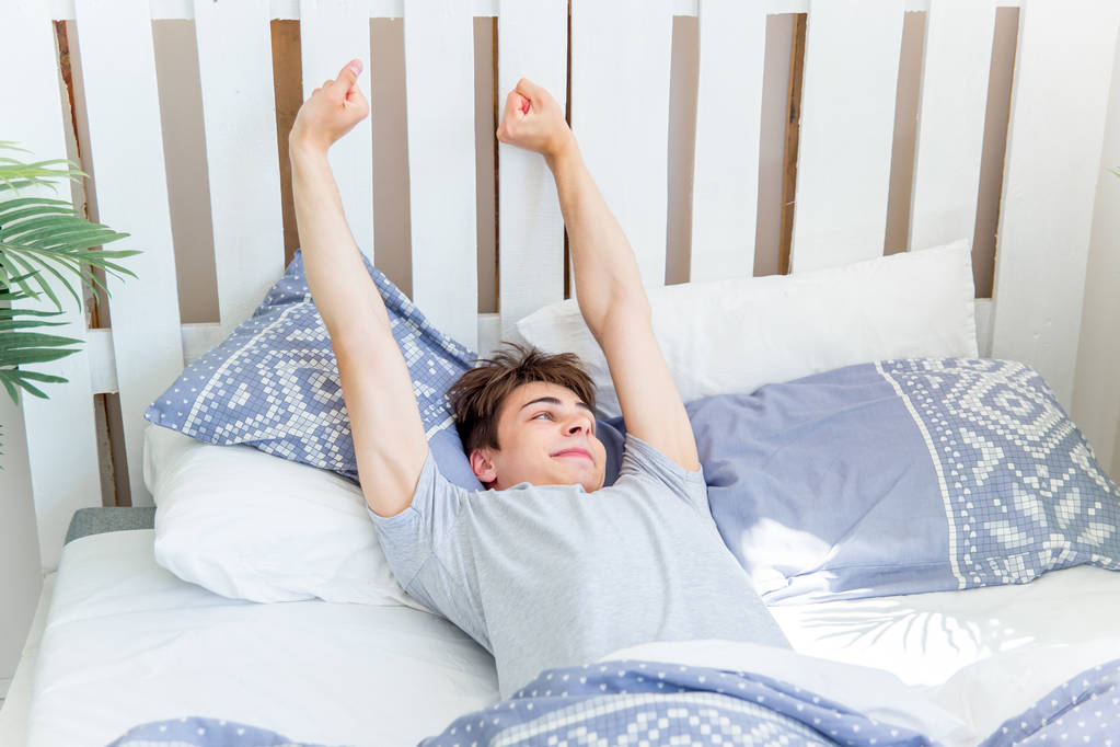 ein junger Mann wacht morgens im Bett auf - Foto, Bild