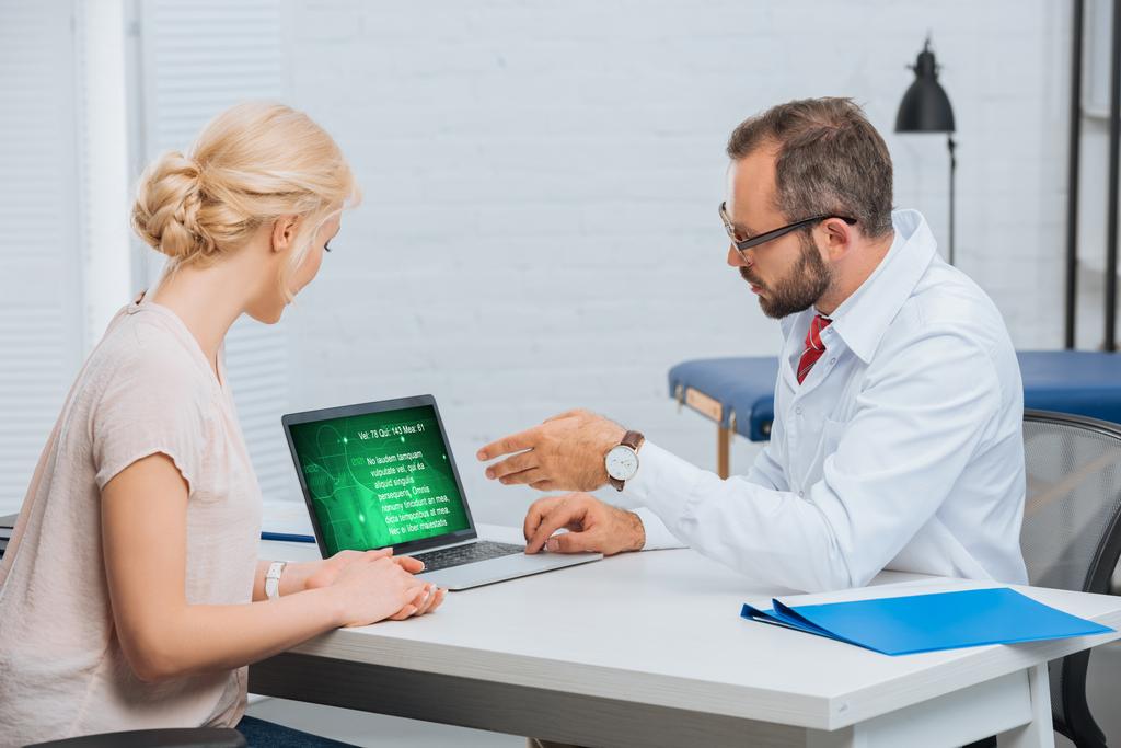 fizyoterapist beyaz ceket konuşmayı bayan hasta ile hastane içinde laptop ile işyerinde - Fotoğraf, Görsel