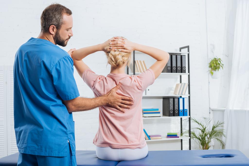 visão traseira do fisioterapeuta fazendo massagem à mulher na mesa de massagem no hospital
 - Foto, Imagem