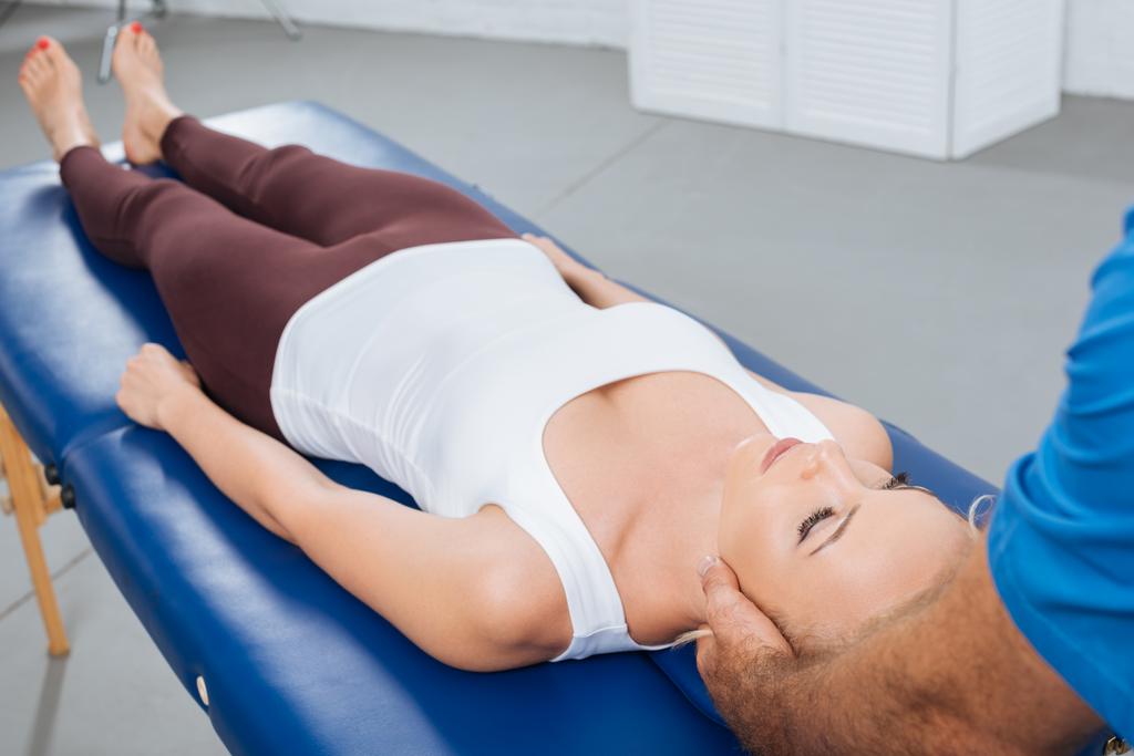 частковий вид фізіотерапевта масажу шиї пацієнта, який лежить на масажному столі в клініці
 - Фото, зображення