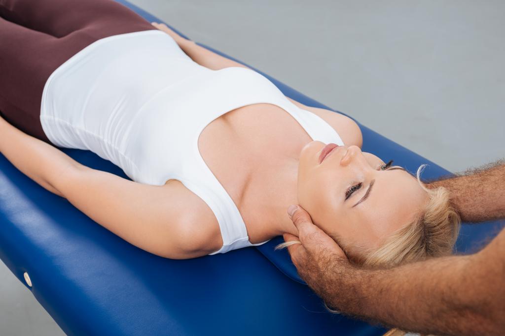 частковий вид фізіотерапевта масажу шиї пацієнта, який лежить на масажному столі в клініці
 - Фото, зображення