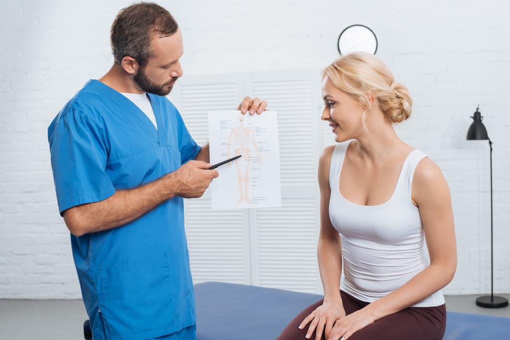 physiothérapeute montrant schéma du corps humain à la femme souriante sur table de massage à l'hôpital
 - Photo, image