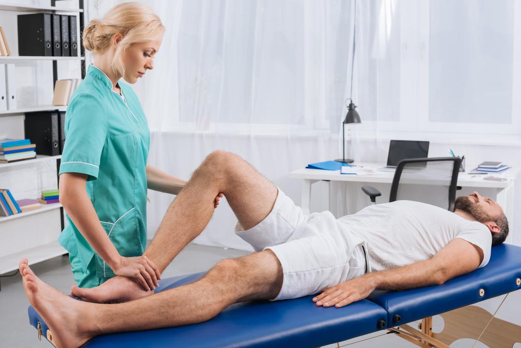 患者の診療所でのマッサージ テーブルの上に脚のマッサージを行う女性マッサージセラピスト - 写真・画像