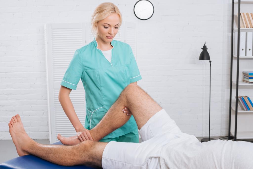 Teilansicht des Chiropraktikers, der Patienten während eines Termins in der Klinik das Bein massiert - Foto, Bild