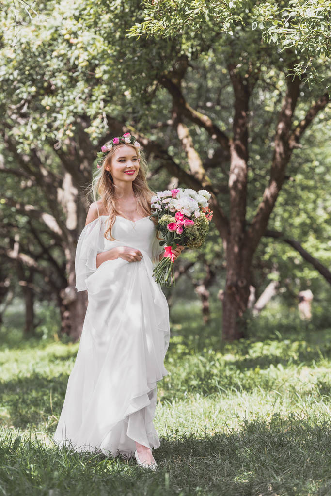 красивая улыбающаяся молодая невеста с свадебным букетом и прогулкой в парке
  - Фото, изображение