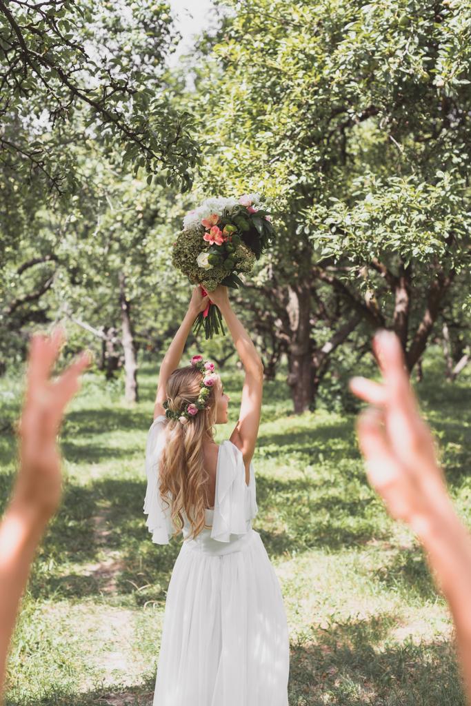 επιλεκτική εστίαση του νεαρή νύφη ρίχνουν γαμήλια ανθοδέσμη στο πάρκο  - Φωτογραφία, εικόνα