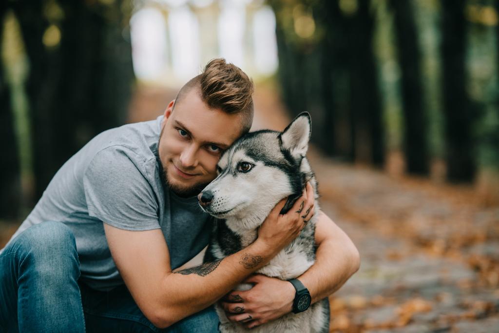 giovane uomo sorridente che abbraccia cane husky nel parco
 - Foto, immagini