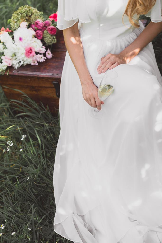 cropped shot of bride holding glass of champagne and sitting on vintage chest    - Photo, Image