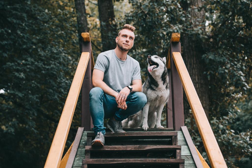 Nuori mies istuu portaissa siperialaisen husky koiran kanssa
  - Valokuva, kuva