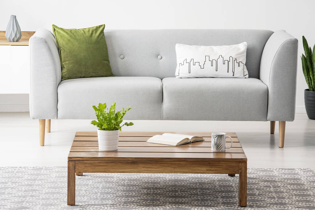 Mesa de café simples, de madeira na frente de um sofá cinza com travesseiros na moda em um interior sala de estar monocromático
 - Foto, Imagem