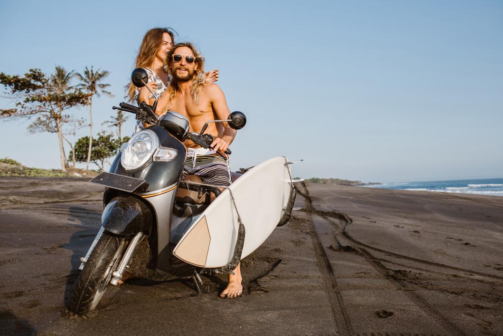 Lachendes Paar mit Motorrad und Surfbrett am Strand von Bali, Indonesien - Foto, Bild