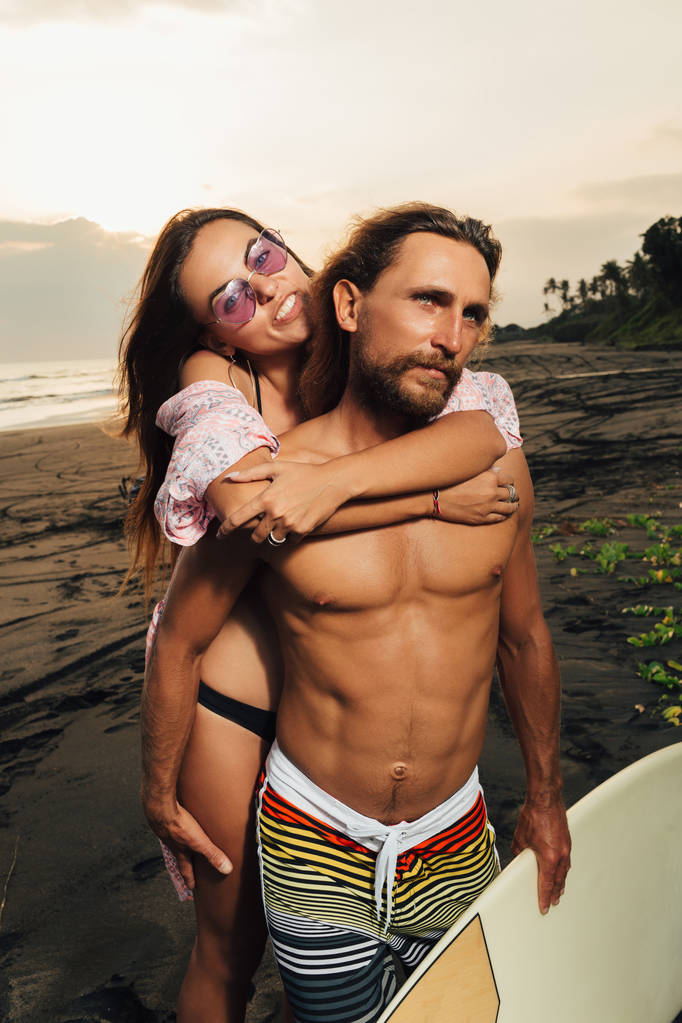 インドネシア、バリ島のビーチでのサーフィン ボードを笑みを浮かべて彼女のハグ彼氏 - 写真・画像