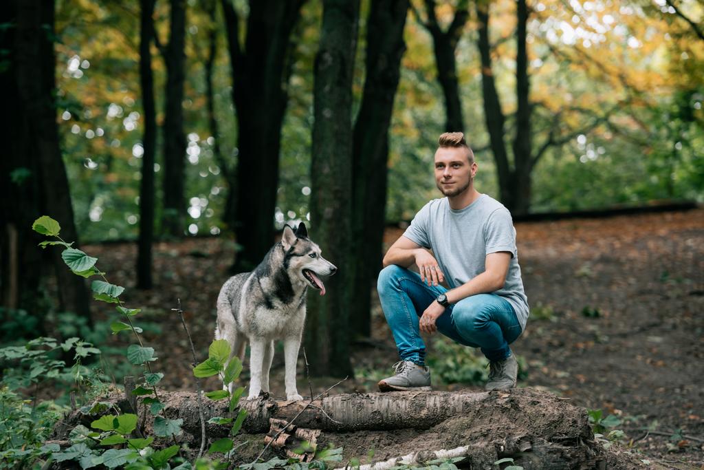 jovem bonito andando com cão husky siberiano na floresta
 - Foto, Imagem
