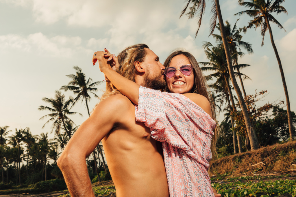вид сбоку улыбающейся пары, обнимающейся на пляже в Бали,
 - Фото, изображение