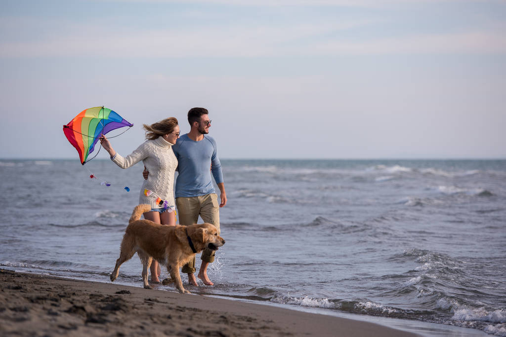 Fiatal pár szórakozik játék-val egy kutya és a Kite a strandon, őszi nap - Fotó, kép