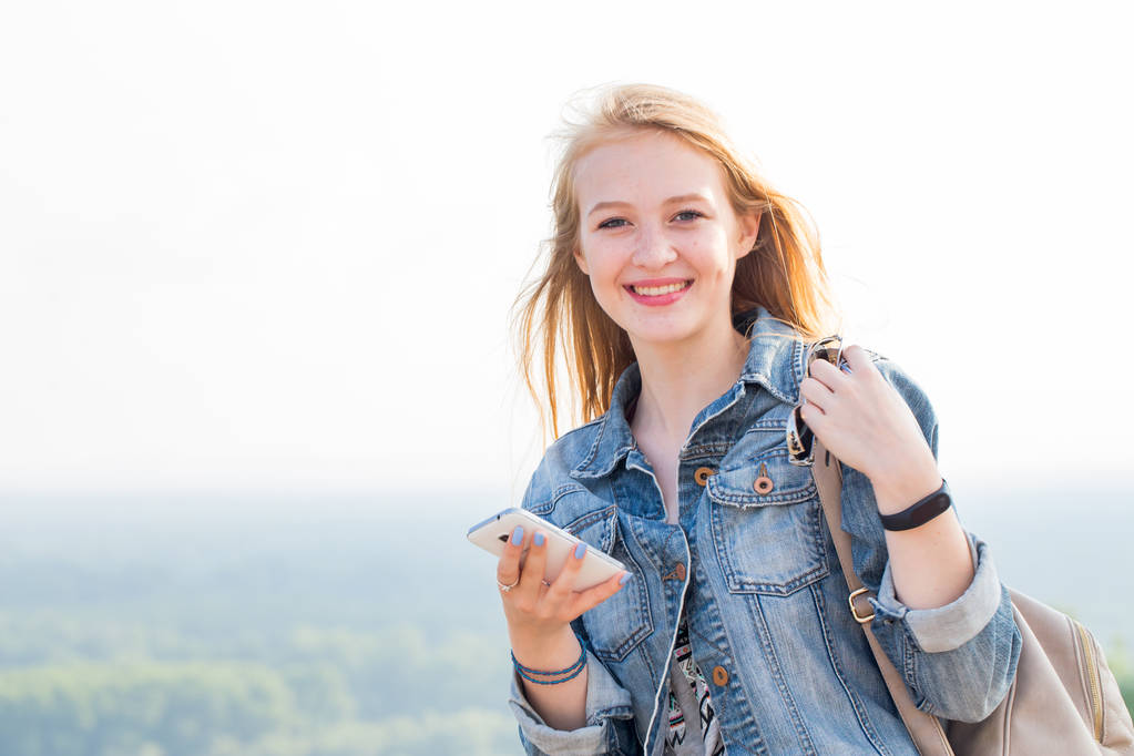 Mujer joven feliz con teléfono inteligente en la mano con sonrisa mirando a la cámara. Viajes, Internet, tecnologías modernas, teléfono, conceptos de estilo de vida
 - Foto, Imagen