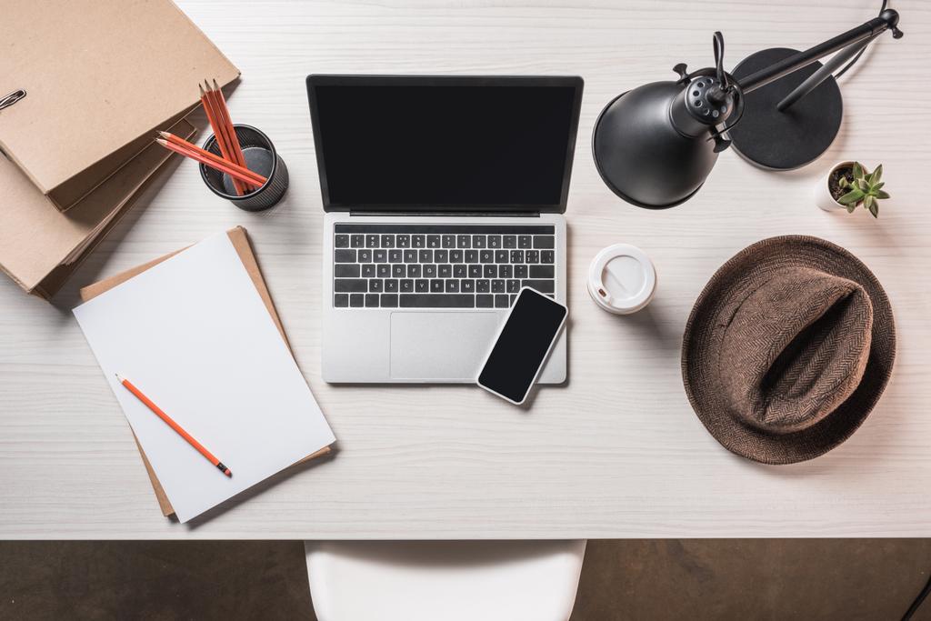 ylhäältä näkymä työpaikalle fedora hattu, kahvikuppi, tyhjä paperi, älypuhelin ja kannettava tietokone pöydällä
  - Valokuva, kuva