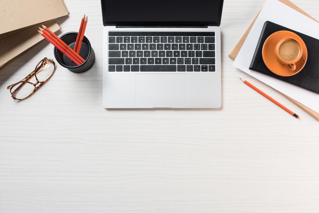 повышенный вид ноутбука с чистым экраном, очки, чашки кофе и канцелярские принадлежности на столе
 - Фото, изображение
