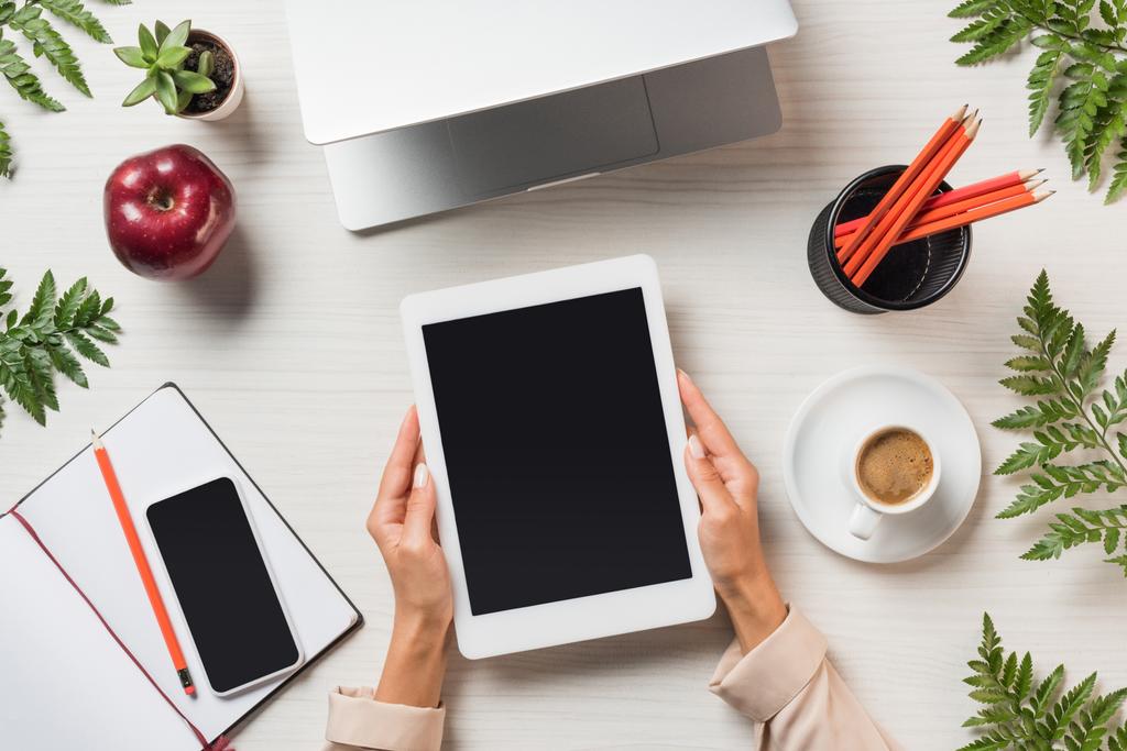visão parcial do freelancer feminino segurando tablet digital com tela em branco à mesa com gadgets e café cercado por folhas de samambaia
  - Foto, Imagem