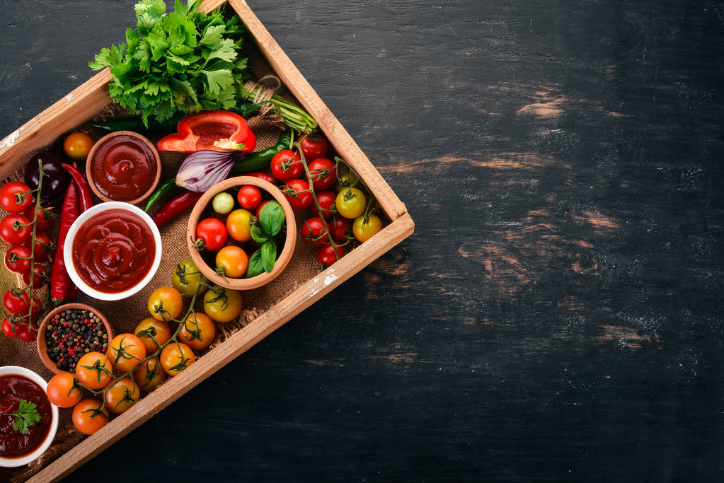 Assortment of tomato sauces in a wooden box. Ketchup. Cherry tomatoes, spices, chili peppers, olive oil, parsley. Top view. - Photo, Image