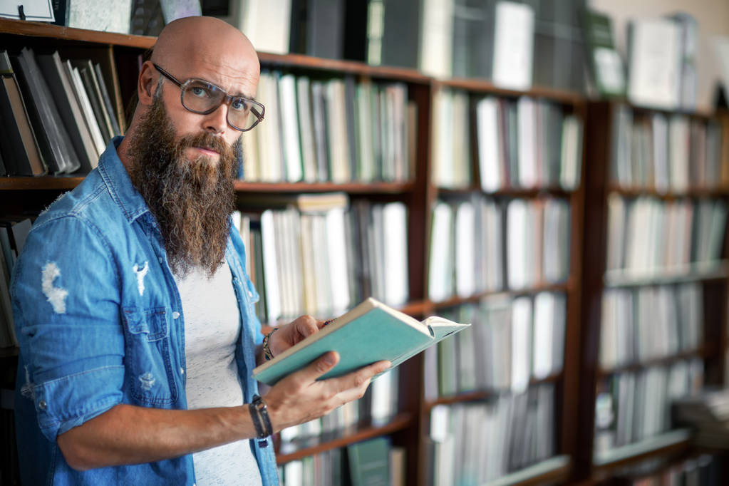 schöner bärtiger Mann mit Brille liest Buch in Bibliothek - Foto, Bild