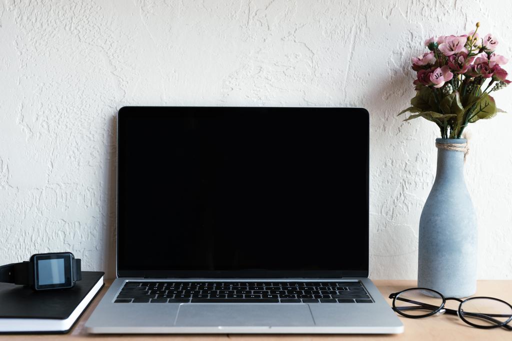 ordinateur portable avec écran blanc, smartwatch, ordinateur portable, lunettes et fleurs dans un vase sur la table
 - Photo, image
