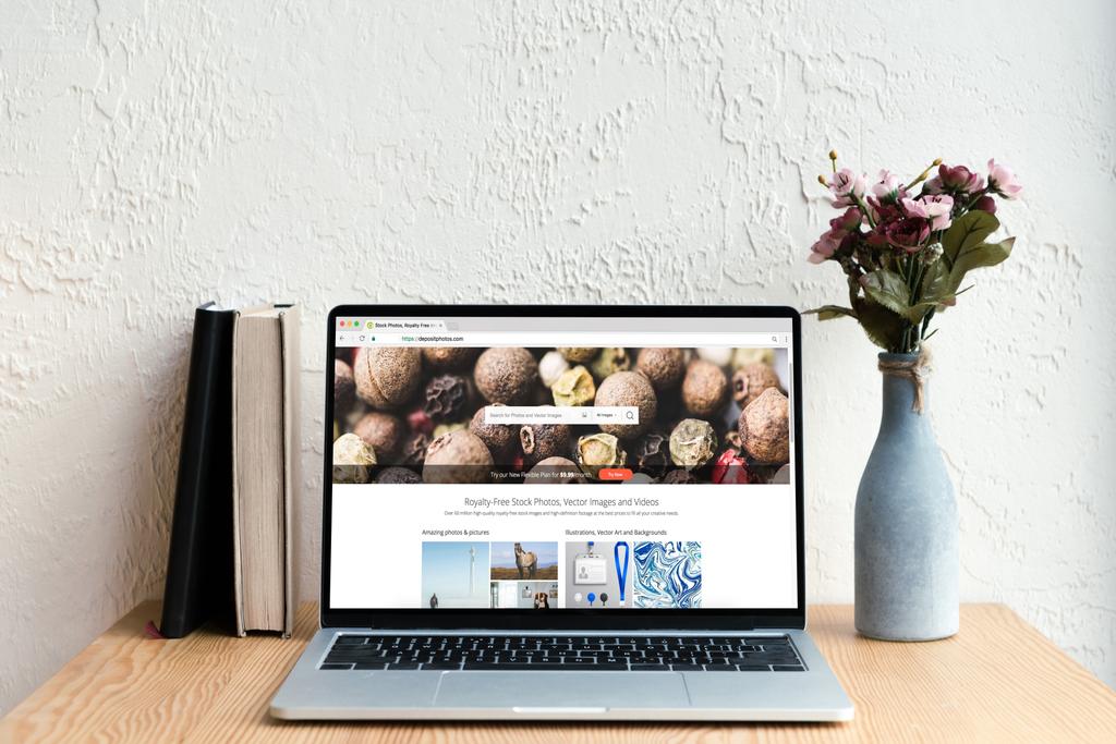 portátil con sitio web depositphotos en pantalla, libros y flores en jarrón sobre mesa de madera
 - Foto, Imagen