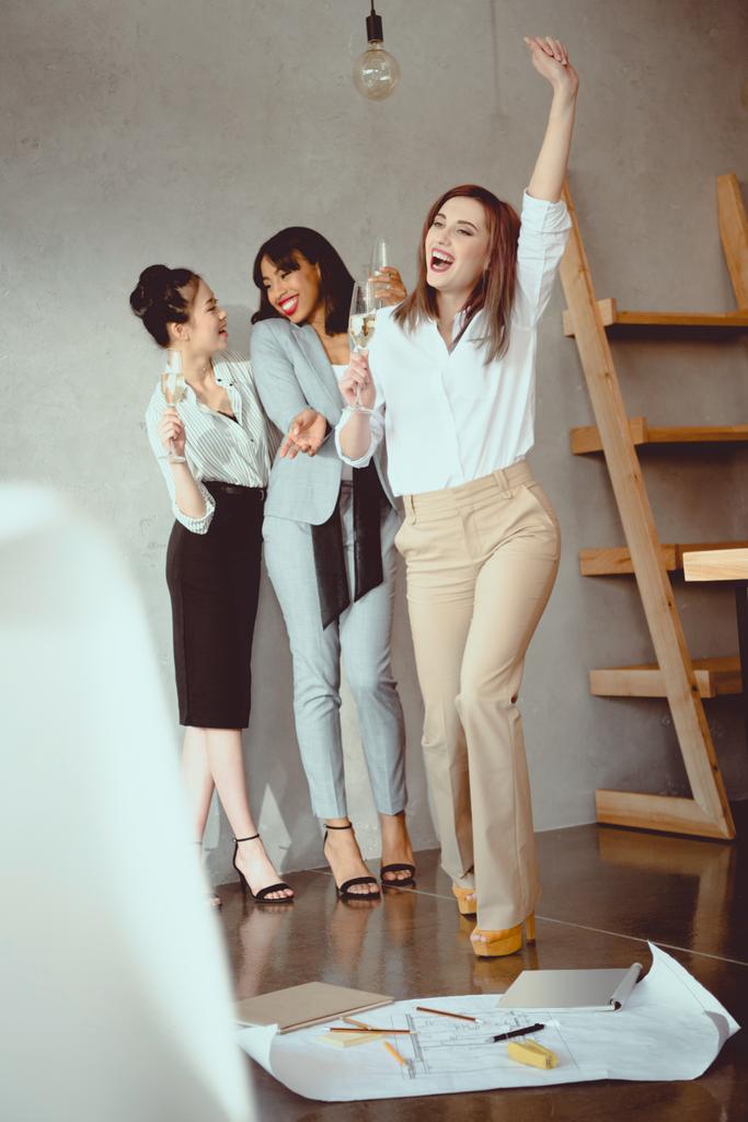 молодые мультиэтнические предпринимательницы празднуют успех и пьют шампанское в помещении
 - Фото, изображение