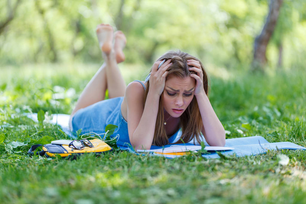 Kaunis nuori nainen kirjoittaa muistikirjaansa puistossa.
 - Valokuva, kuva