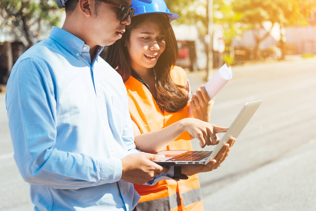 Homme et femme ingénieur asiatique avec le casque de sécurité bleu réunion sur le site de construction avec des plans et un ordinateur portable
. - Photo, image