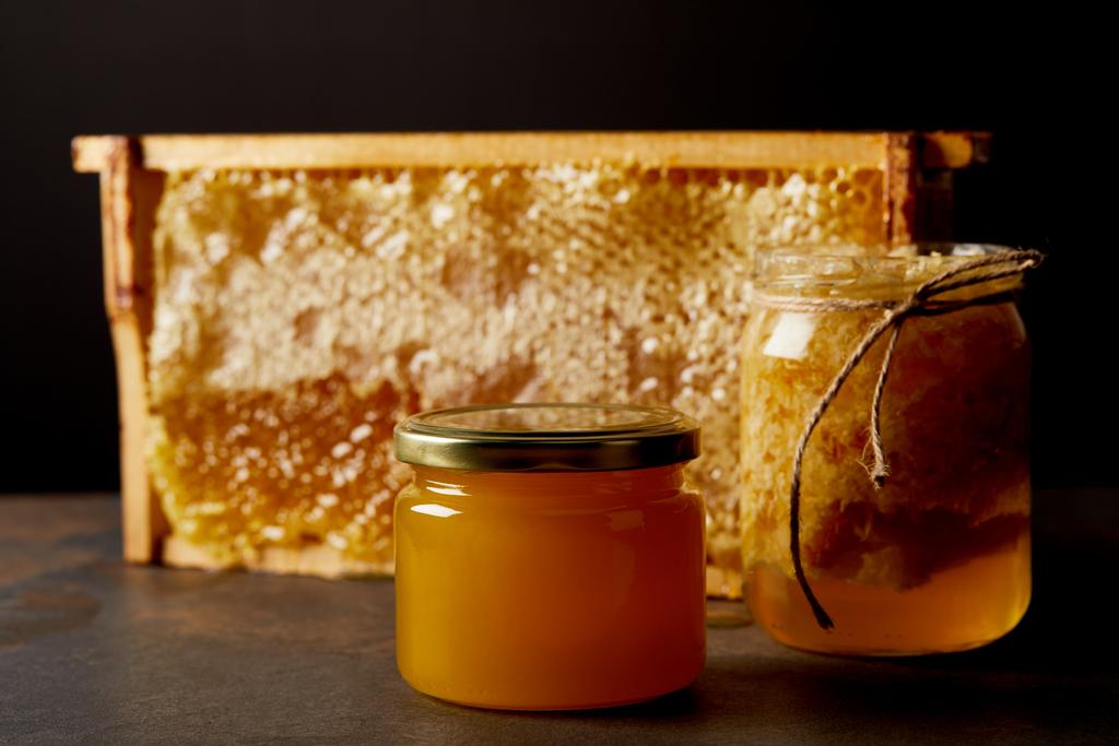 zár megjelöl kilátás üvegedények, mézzel és méhviasz szutykos asztallapra a fekete háttér előtt - Fotó, kép